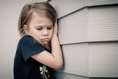 Portrait of sad little girl sitting near wall in the day time